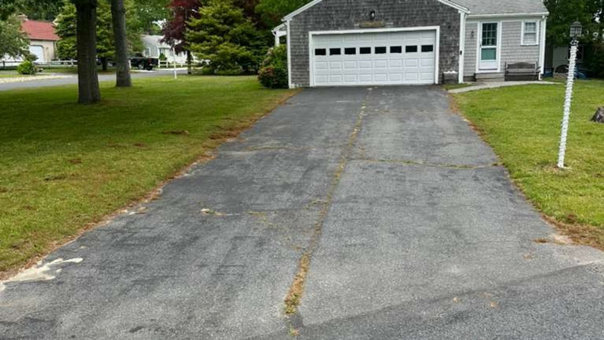 Weathered residential driveway before sealcoating with house and driveway context